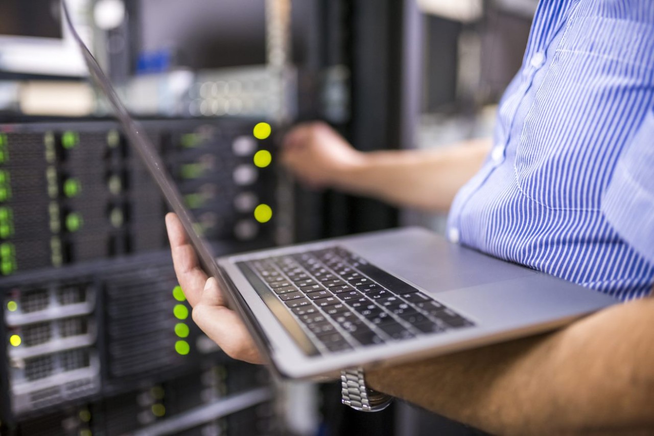 Man in server room holding a laptop and touching a piece of rack equipment