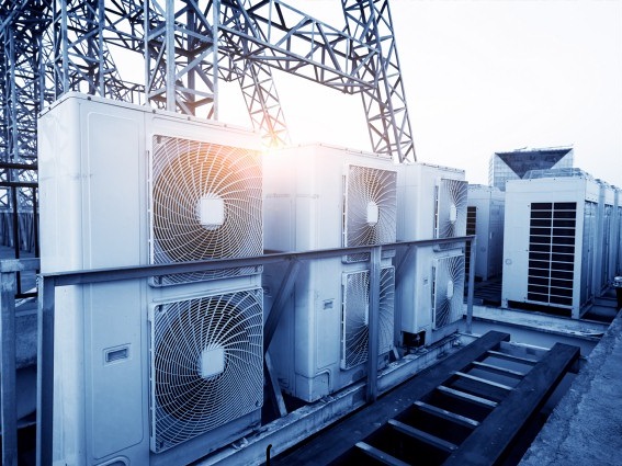 Air conditioner units (HVAC) on a roof of industrial building with blue sky and clouds in the background.
