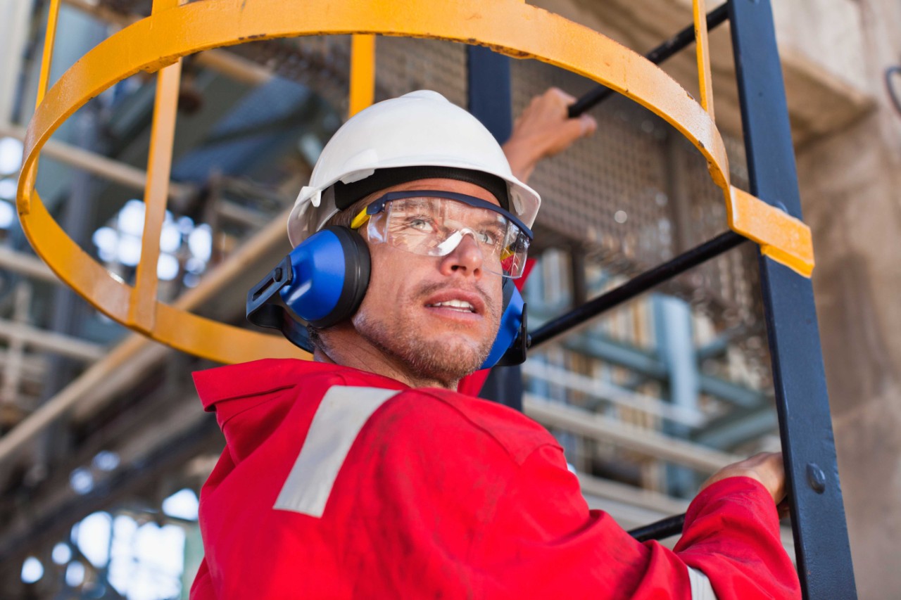 Man with safety glasses, hardhat and ear protection climbing a ladder