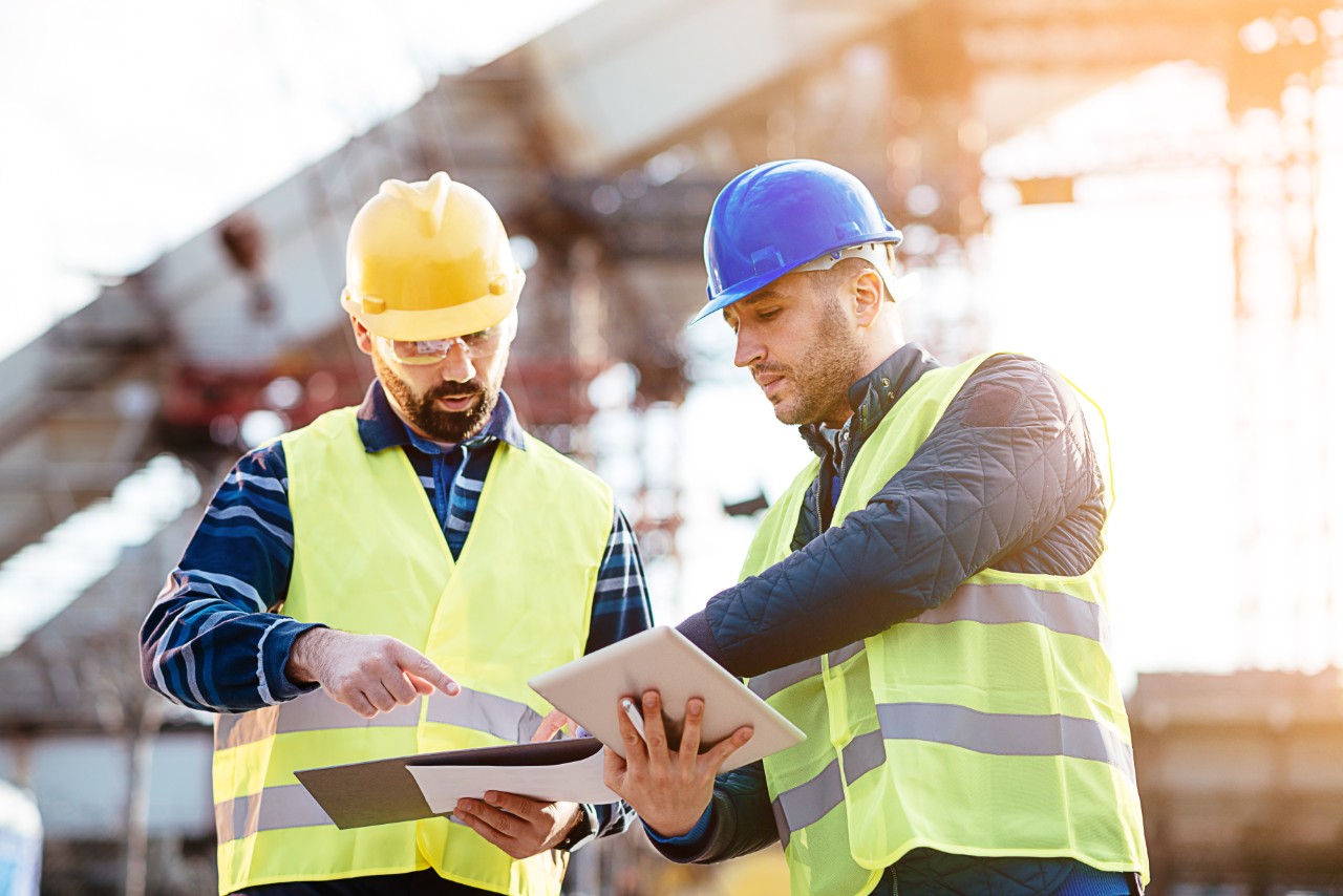 Two experts engineers in protective helmets and fluorescent vests showing the construction site and building activities after the successful project phase. 