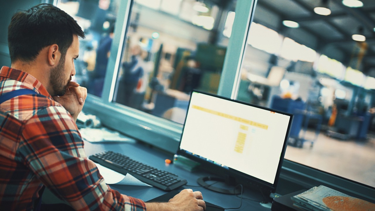 Closeup side view of a control room at a modern industrial production line with a control person in charge keeping track of the process on a computer.