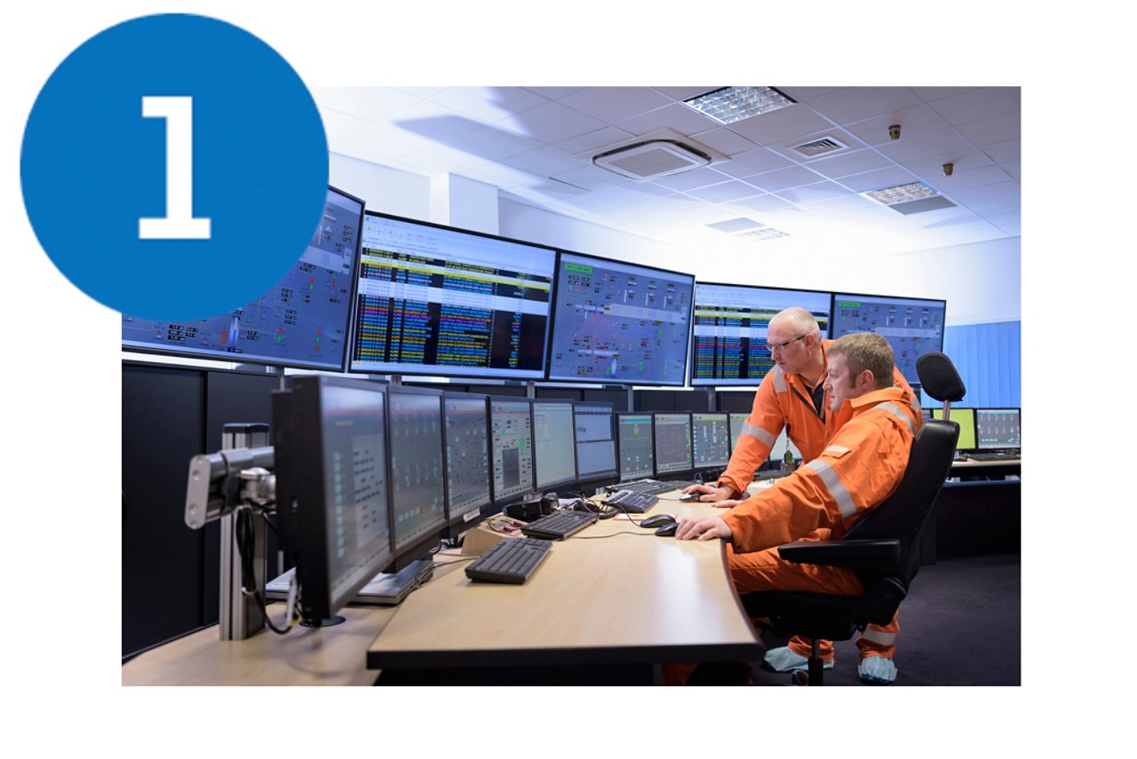 Two male workers (engineers) working in a power station control room. 