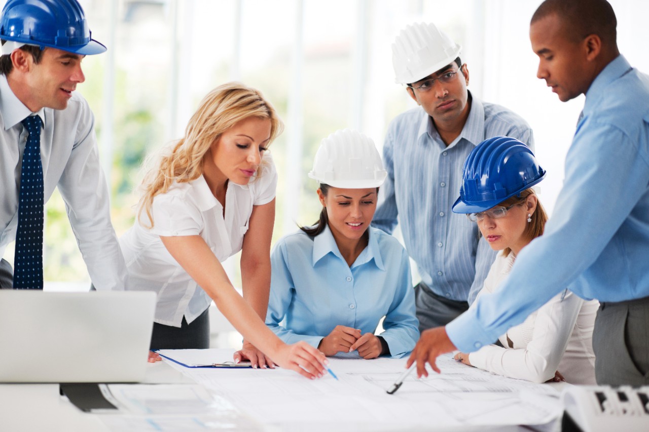 Group of successful architects talking about the project. They are wearing protective helmets.   