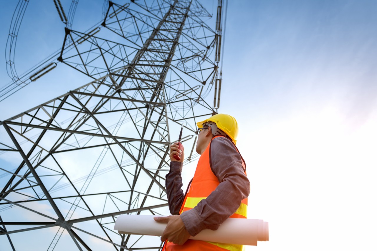 Construction worker checking location site near to High voltage tower 