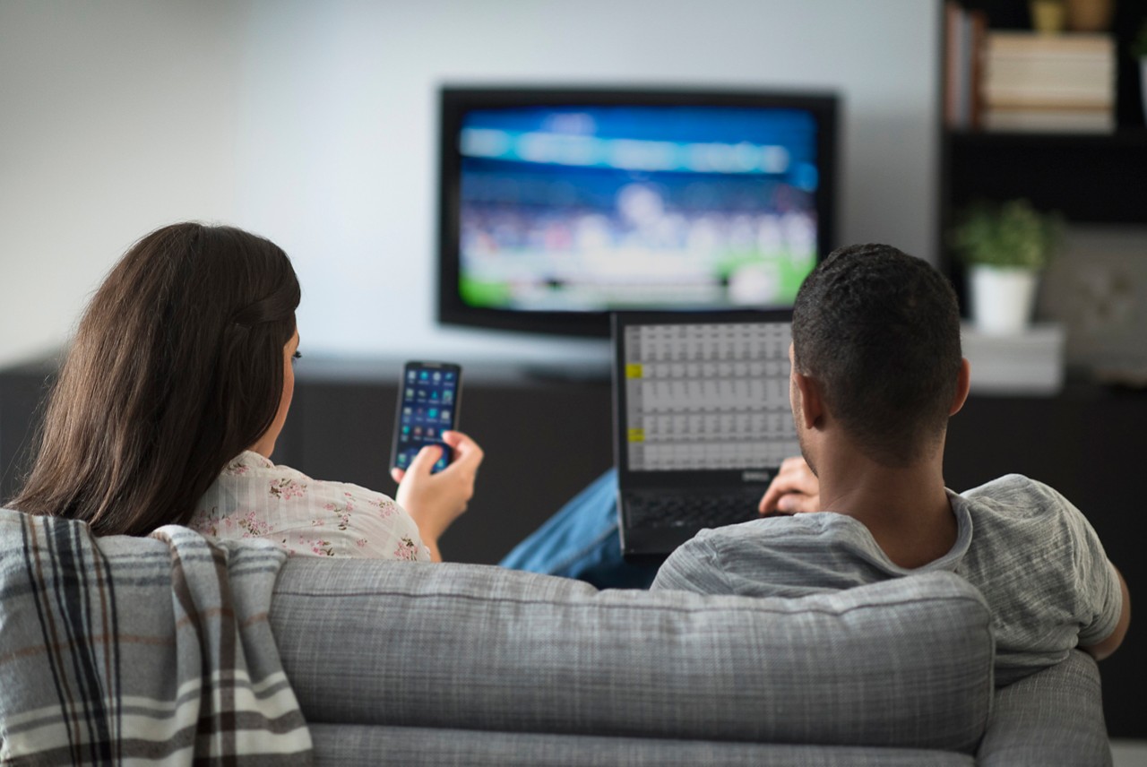 couple-in-living-room-using-laptop-cell-phone-getty-539668551